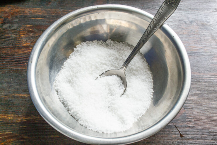 Starting the Spiced Salt Base with Coarse Sea Salt A white bowl being filled with coarse sea salt from a measuring cup.