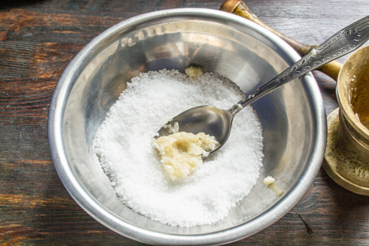 Using a Mortar and Pestle to Make Garlic Paste with Salt A mortar and pestle being used to grind fresh garlic cloves with salt into a fine paste.