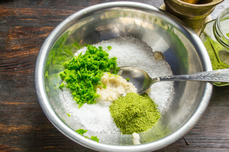 Adding Aromatic Dried Dill to the Spice Blend Dried dill being sprinkled into the bowl with salt and garlic scapes.