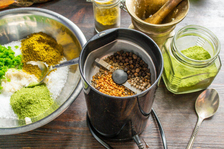 Grinding Whole Spices for Maximum Freshness and Aroma A coffee grinder filled with a mix of whole spices: fenugreek, coriander, caraway, and black pepper.