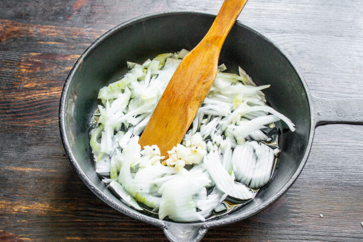 Sautéing onions and garlic in olive oil to build the flavor base for the ragout. Chopped onion and garlic being sautéed in a cast-iron skillet with olive oil.