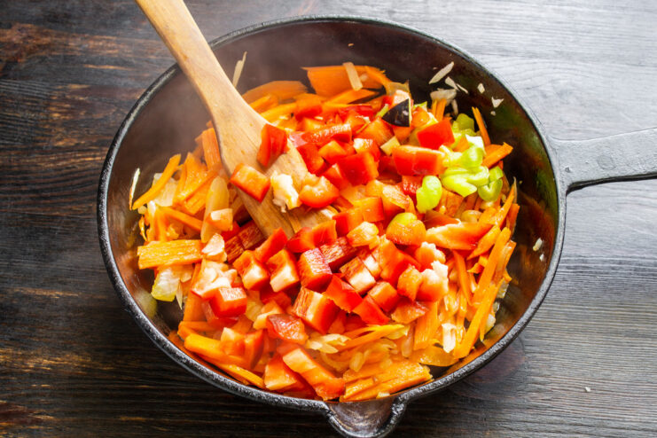 Dicing a red bell pepper for the vegetable ragout. A hand dicing a red bell pepper on a cutting board for the ragout.