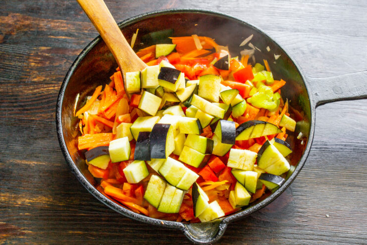 Cutting a fresh eggplant into small cubes for the ragout. A close-up of a fresh eggplant being diced into small cubes on a cutting board.