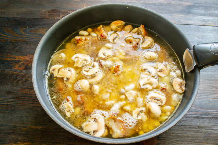 Adding boiling water to cover the ingredients for simmering. Pouring boiling water into a skillet with beans, ribs, and vegetables.