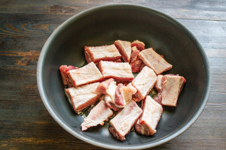 Preparing the pork ribs by cutting them into single-rib portions. A rack of pork ribs on a cutting board being cut into individual pieces.