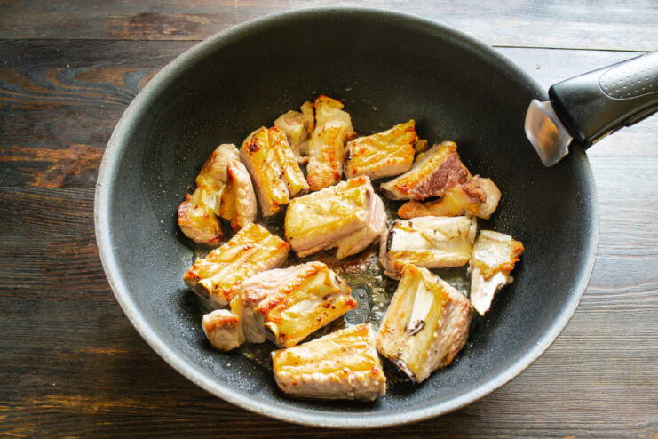 Searing the ribs until golden brown to lock in flavor and juices. Pork ribs sizzling and browning in a hot skillet.