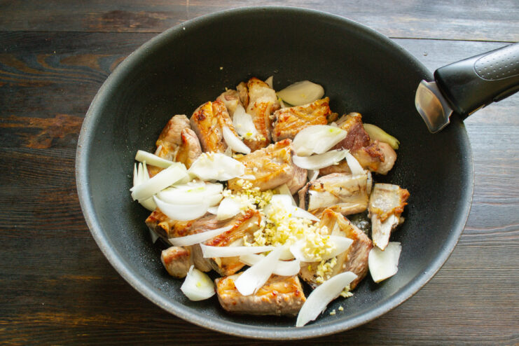 Mincing fresh garlic to add aromatic depth to the stew. Freshly minced garlic cloves on a wooden cutting board.