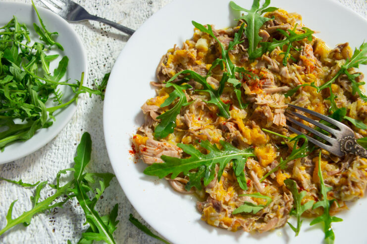 A white bowl filled with creamy pumpkin and turkey stew, topped with fresh arugula.