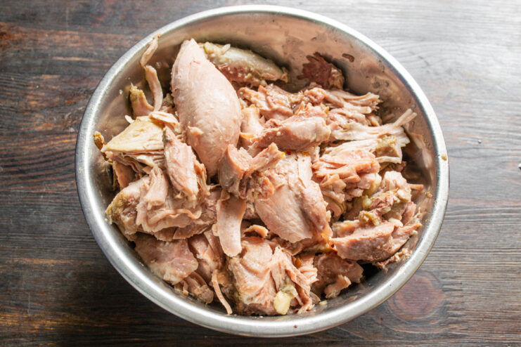 Preparing the Turkey for the Stew Pieces of cooked turkey meat being shredded on a wooden cutting board.