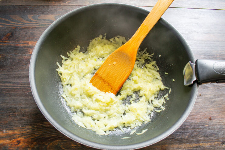 Sautéing Aromatics for the Stew Base Chopped onion and garlic being sautéed in a deep skillet until translucent.