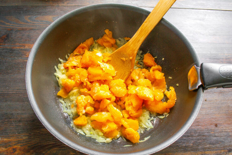Adding Pumpkin to the Skillet Diced pumpkin being added to a skillet with sautéed onions and garlic.