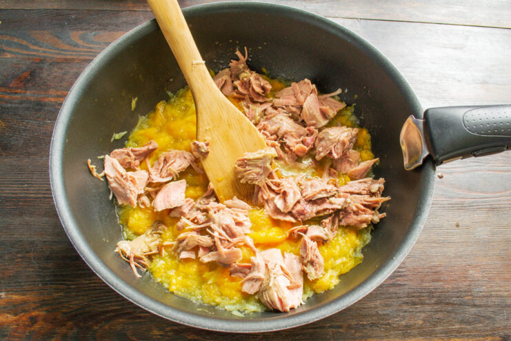 Adding Cooked Turkey to the Stew Shredded cooked turkey being added to the simmering pumpkin in a skillet.