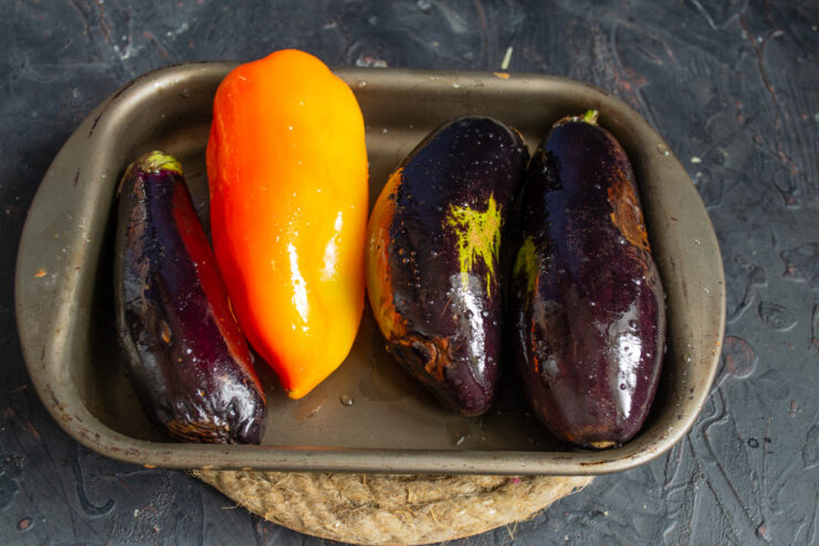 Preparing Vegetables for Roasting: Eggplants and Bell Peppers on a Baking Sheet Whole eggplants and bell peppers coated in oil on a baking sheet, ready to be roasted.