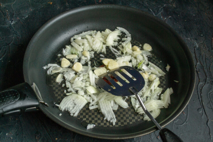Sautéing Aromatics: Starting the Ragout Base with Onions and Garlic Chopped onions and sliced garlic being sautéed in olive oil in a skillet.