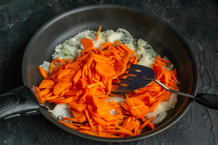 Adding Julienne Carrots to the Skillet for Sweetness and Color Julienned carrots being added to the skillet with sautéed onions and garlic.