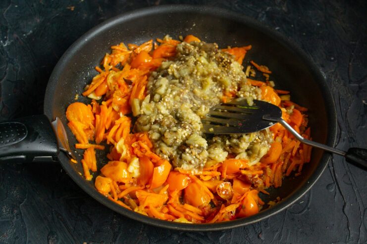 Adding the Smoky Pulp of Roasted Eggplant to the Ragout Chopped roasted eggplant pulp being added to the vegetable mixture in the skillet.