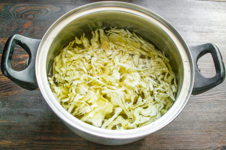 How to Perfectly Shred Cabbage for Soup Close-up of white cabbage being shredded into thin strips on a cutting board.