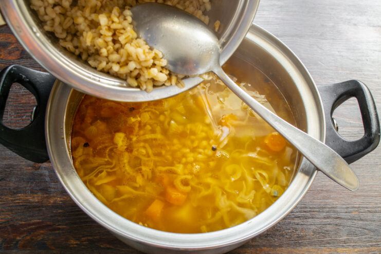Adding Cooked Pearl Barley for a Hearty Texture Cooked pearl barley being added to the pot of Rassolnik soup.