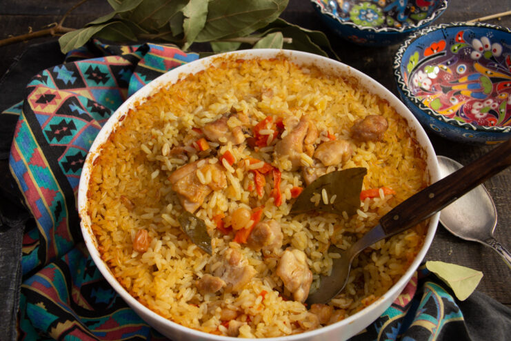 A serving of fluffy chicken plov with carrots and raisins in a white bowl.