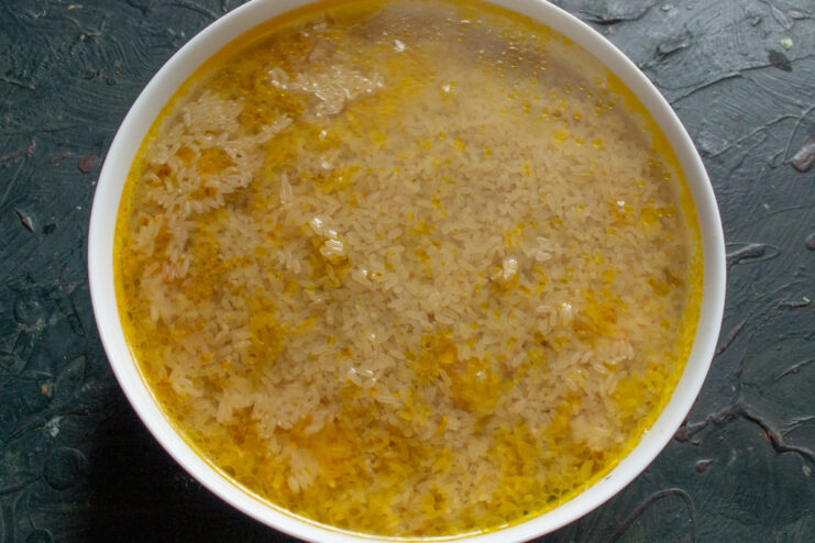 Carefully adding boiling water to the plov before baking. Boiling water being carefully poured into the baking dish over the rice.