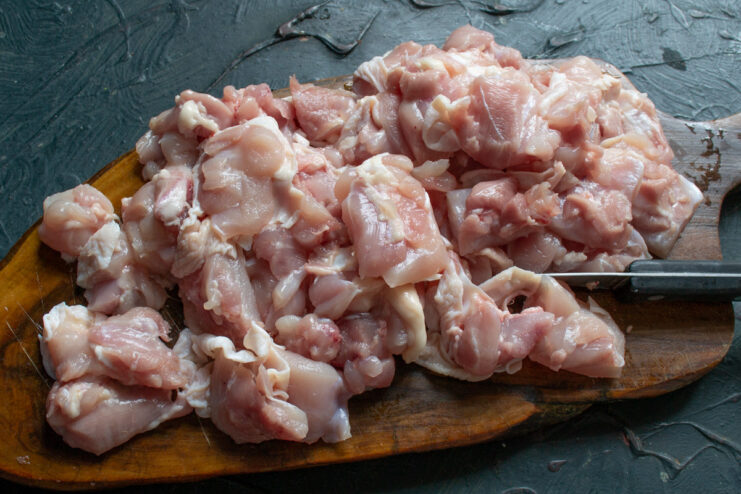 Cutting chicken thighs into even cubes for the plov. Raw chicken thigh meat being cut into cubes on a cutting board.