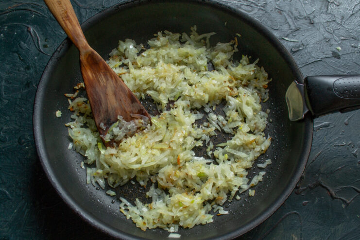 How to finely chop an onion for the plov base. A hand holding a knife, finely chopping a yellow onion on a cutting board.