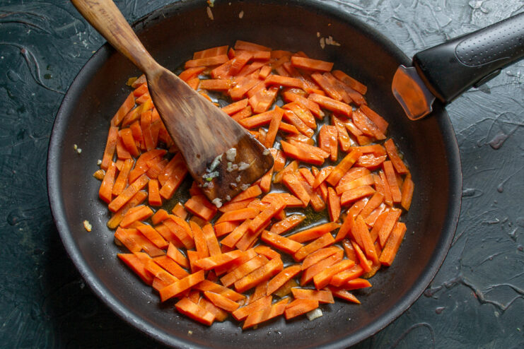 Sautéing carrot sticks until tender-crisp for the plov. Carrot sticks being sautéed in a skillet with oil.