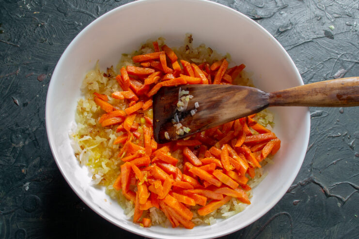 Layering the sautéed vegetables as the first layer in the baking dish. Sautéed onions and carrots layered at the bottom of a glass baking dish.