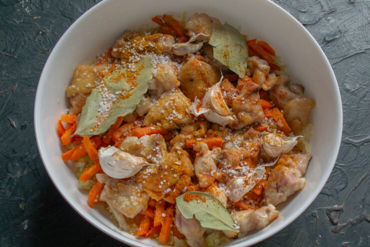 Adding aromatics like crushed garlic and bay leaves for extra flavor. Crushed garlic cloves and bay leaves being added to the chicken and vegetables in the baking dish.