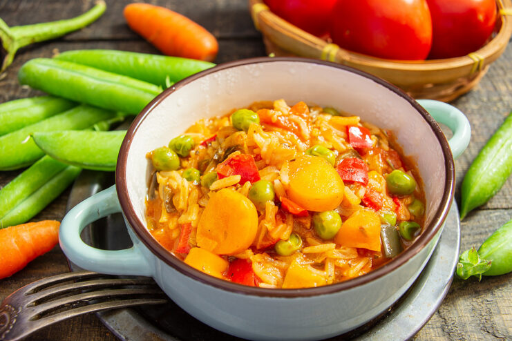 A white bowl filled with colorful ratatouille with rice, garnished with fresh herbs.