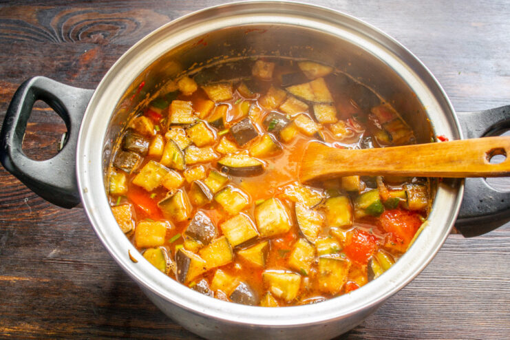 Pouring hot vegetable broth into the pot to cook the rice and vegetables. Hot vegetable broth being poured from a measuring cup into the pot of ratatouille.