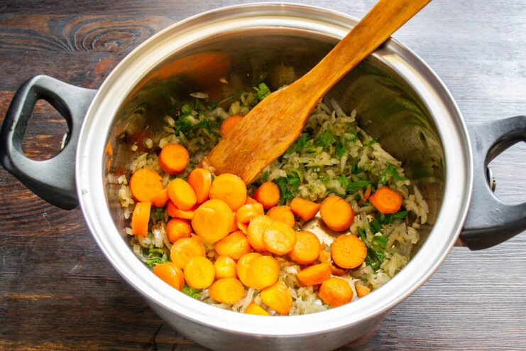 Adding sliced carrots to the sautéed vegetables in the pot. Sliced carrots being added to a pot with sautéed onions and celery.