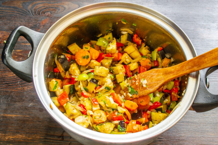 Adding diced eggplant to the pot with other vegetables for the ratatouille. Diced purple eggplant being added to a pot of cooking vegetables.
