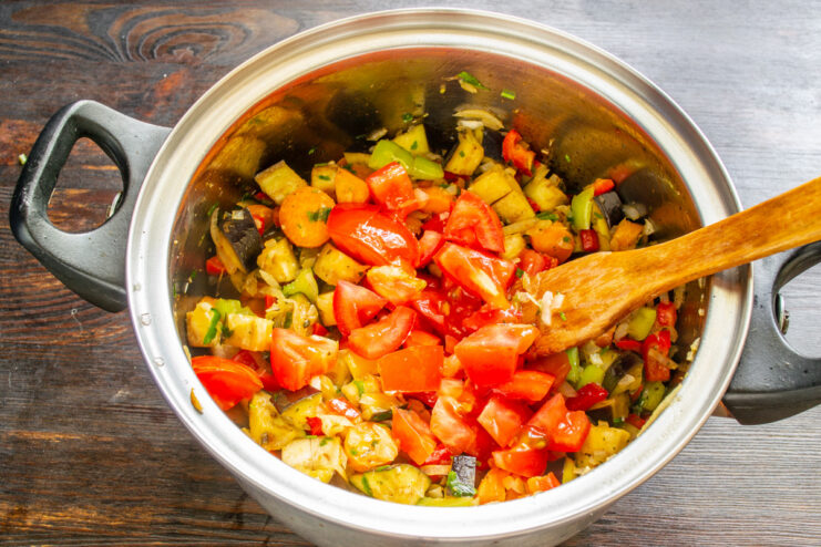 Adding fresh, chopped tomatoes to the vegetable stew for a rich sauce. Finely chopped fresh tomatoes being added to the pot of ratatouille.