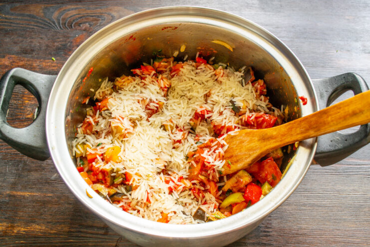 Adding uncooked long-grain white rice directly into the pot with the vegetables. Pouring long-grain white rice into the pot with the simmering vegetables.