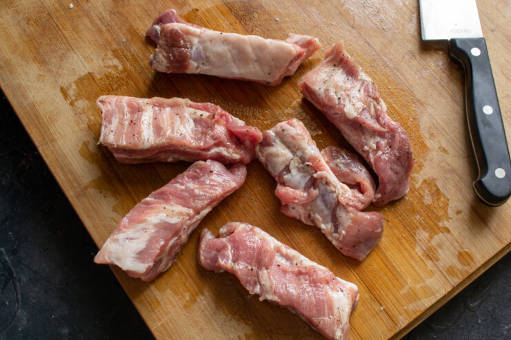 Seasoning the Ribs: Rubbing with Oil and Pepper Hands rubbing oil and black pepper into raw pork ribs.