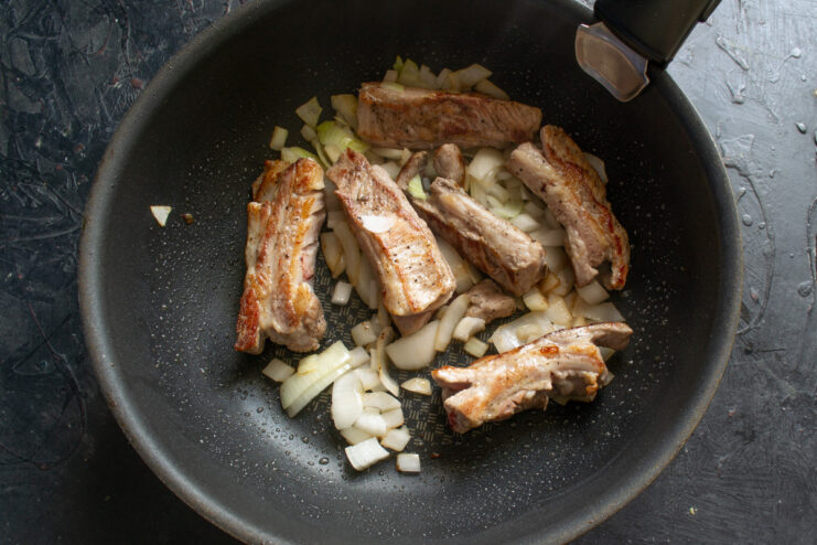 Building Flavor: Adding Onions to the Searing Ribs Chopped onions being added to a skillet with searing pork ribs.
