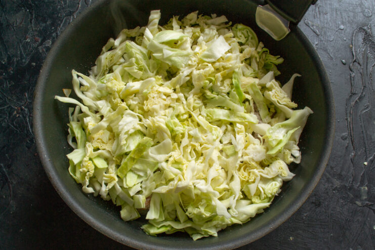 Combining Ingredients: Adding Cabbage to the Skillet Shredded cabbage being added to the skillet with ribs and onions.
