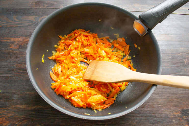 Sautéing Onions and Carrots to Build Flavor Diced onions and grated carrots being sautéed in a frying pan.