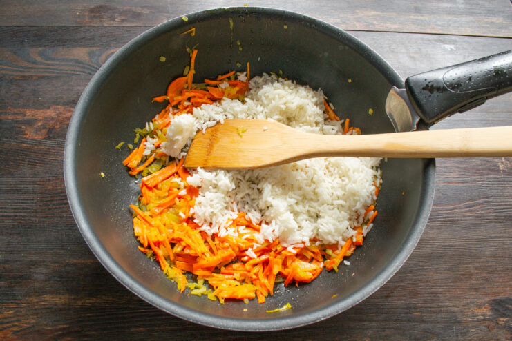 Combining Cooked Rice with Sautéed Vegetables Cooked white rice being added to a pan with sautéed carrots and onions.