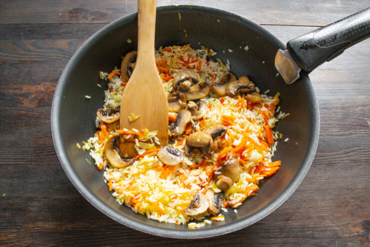 Adding Savory Fried Mushrooms to the Rice Mixture Fried mushrooms being added to the rice and vegetable mixture in a pan.