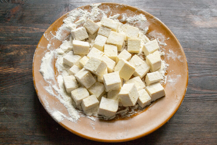 How to Cut Tofu into Cubes for Frying A block of plain tofu being cut into even cubes on a cutting board.