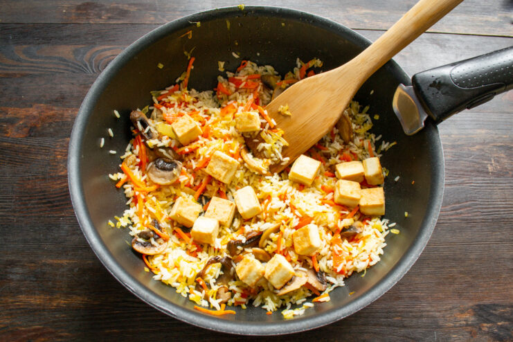 Combining All Ingredients for the Final Dish Golden fried tofu being mixed with rice, mushrooms, and vegetables in a pan.