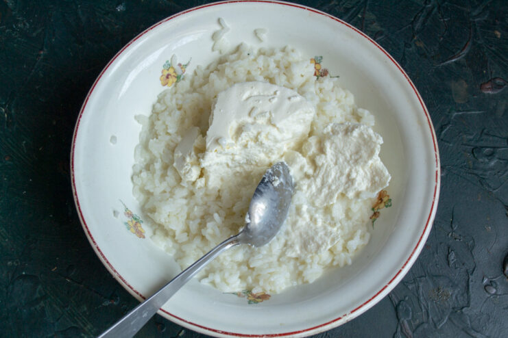 Step 2: Adding ricotta cheese to the rice mixture for a rich and tender texture. Ricotta cheese being added to a bowl of rice and milk mixture.