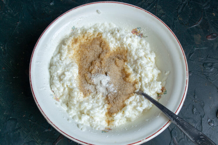 Step 3: Seasoning the casserole batter with sugar and cinnamon for sweetness and warmth. Sugar and cinnamon being added to the rice and ricotta mixture in a bowl.