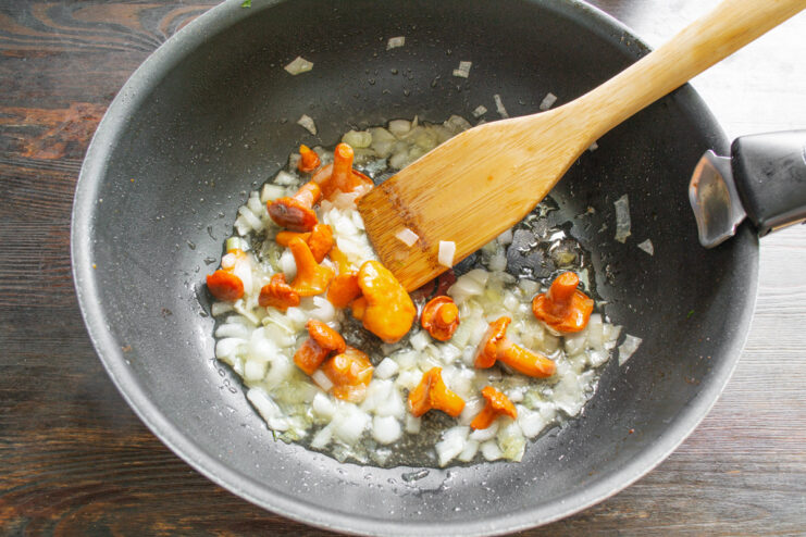 Cooking Chanterelle Mushrooms with Onions for Risotto Fresh chanterelle mushrooms being sautéed with onions in a large skillet.