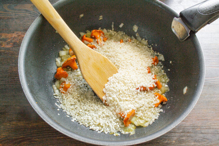 Toasting the Arborio Rice for a Perfect Risotto Texture Short-grain Arborio rice being added to the skillet with sautéed mushrooms and onions.