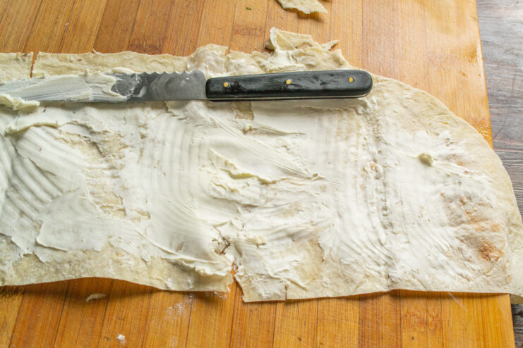 Spreading a layer of cream cheese on the lavash A hand spreading white cream cheese evenly over a sheet of lavash bread.