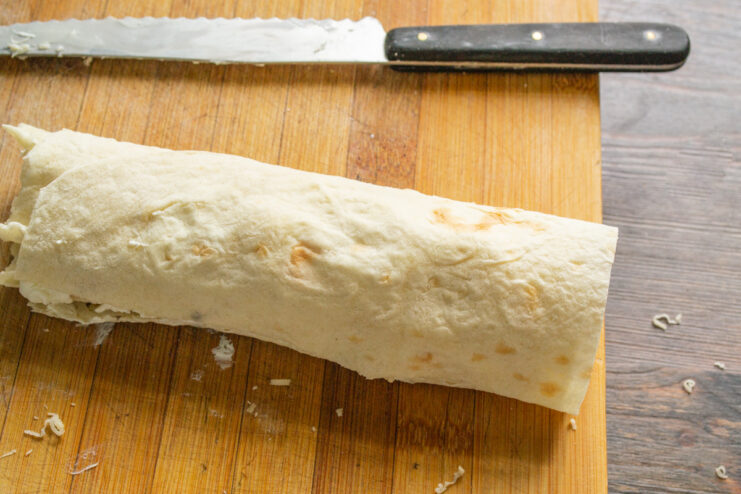 How to roll the lavash with cheese filling A tightly rolled lavash filled with three types of cheese on a cutting board.