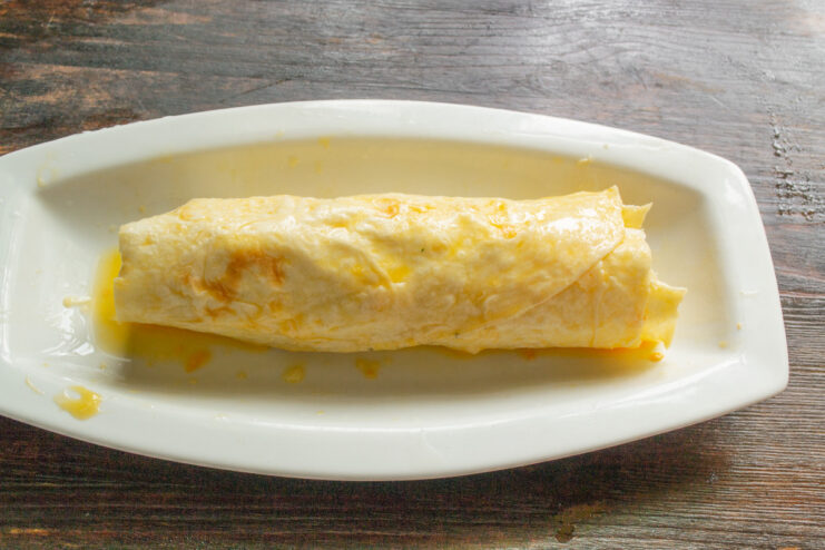Coating the lavash roll in egg wash before breading A lavash roll being dipped into a long dish with beaten egg.